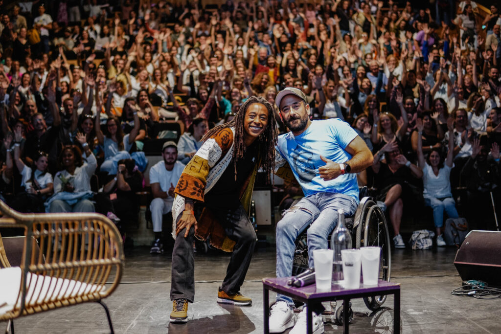 Deux intervenant·es en pleine conférence sur scène, devant une salle comble et enthousiaste.